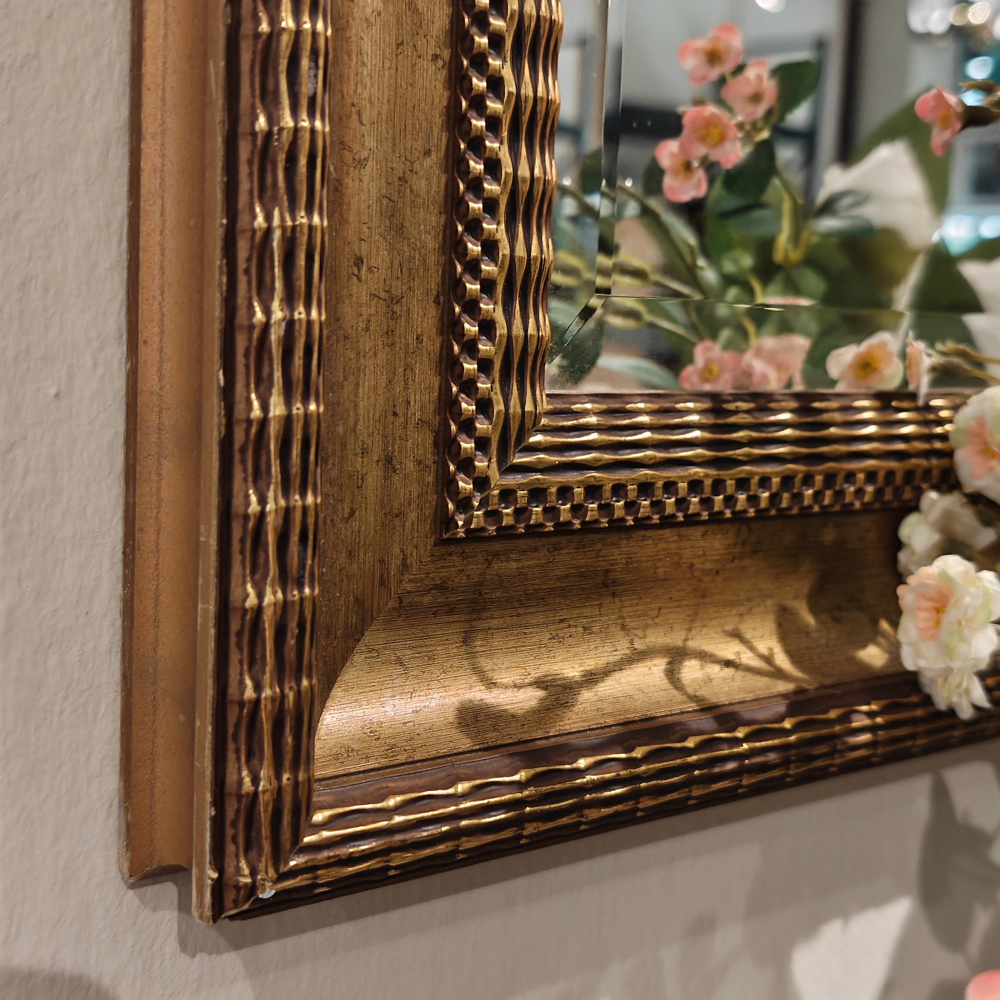 Decorative gold-framed mirror on a wall with floral decorations.