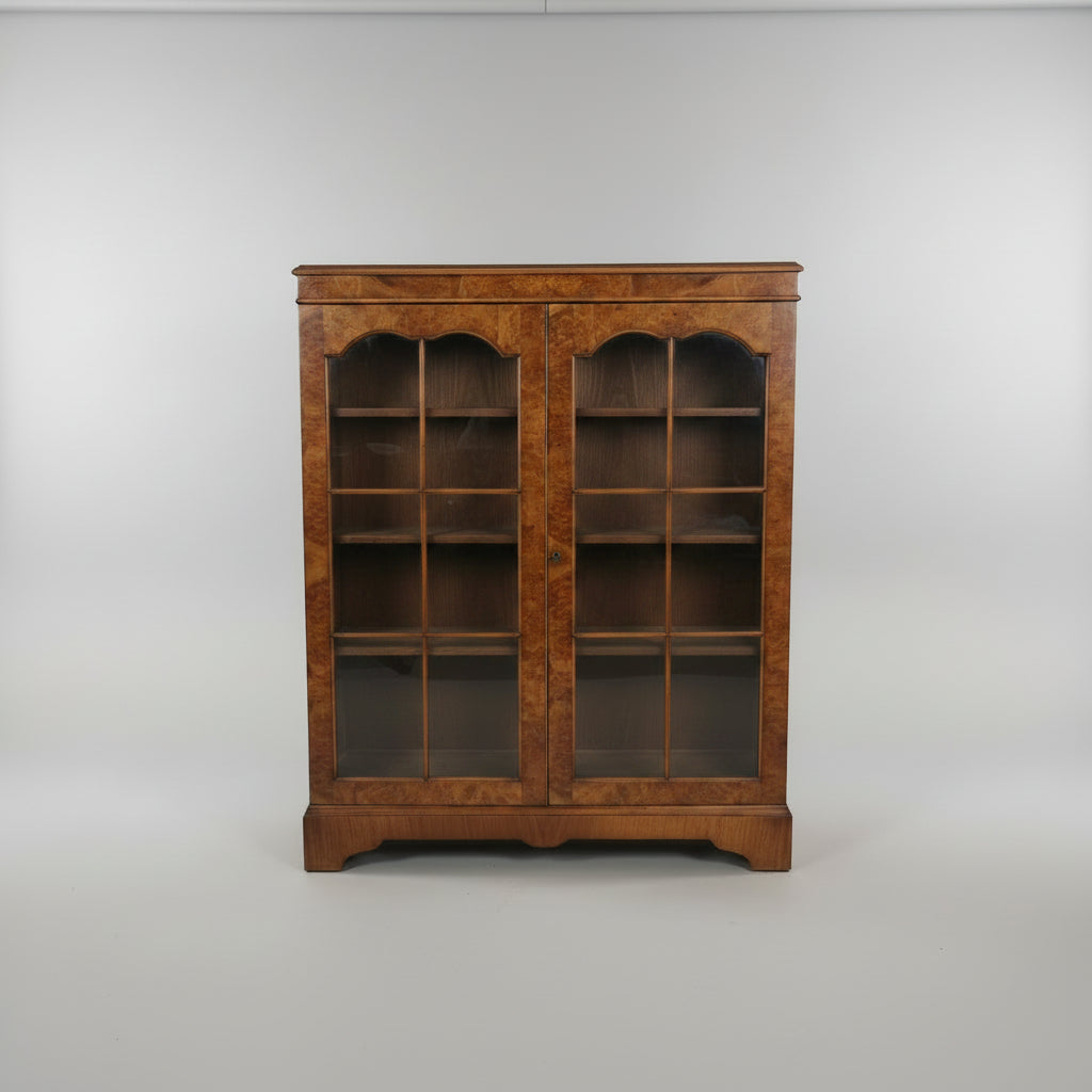A vintage wooden china cabinet with glass doors, filled with white teacups, saucers, and plates, photographed in a furniture store.