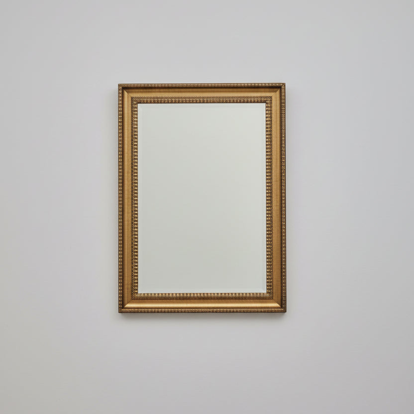 Decorative mirror with gold frame on a wooden dresser with flowers and a book.