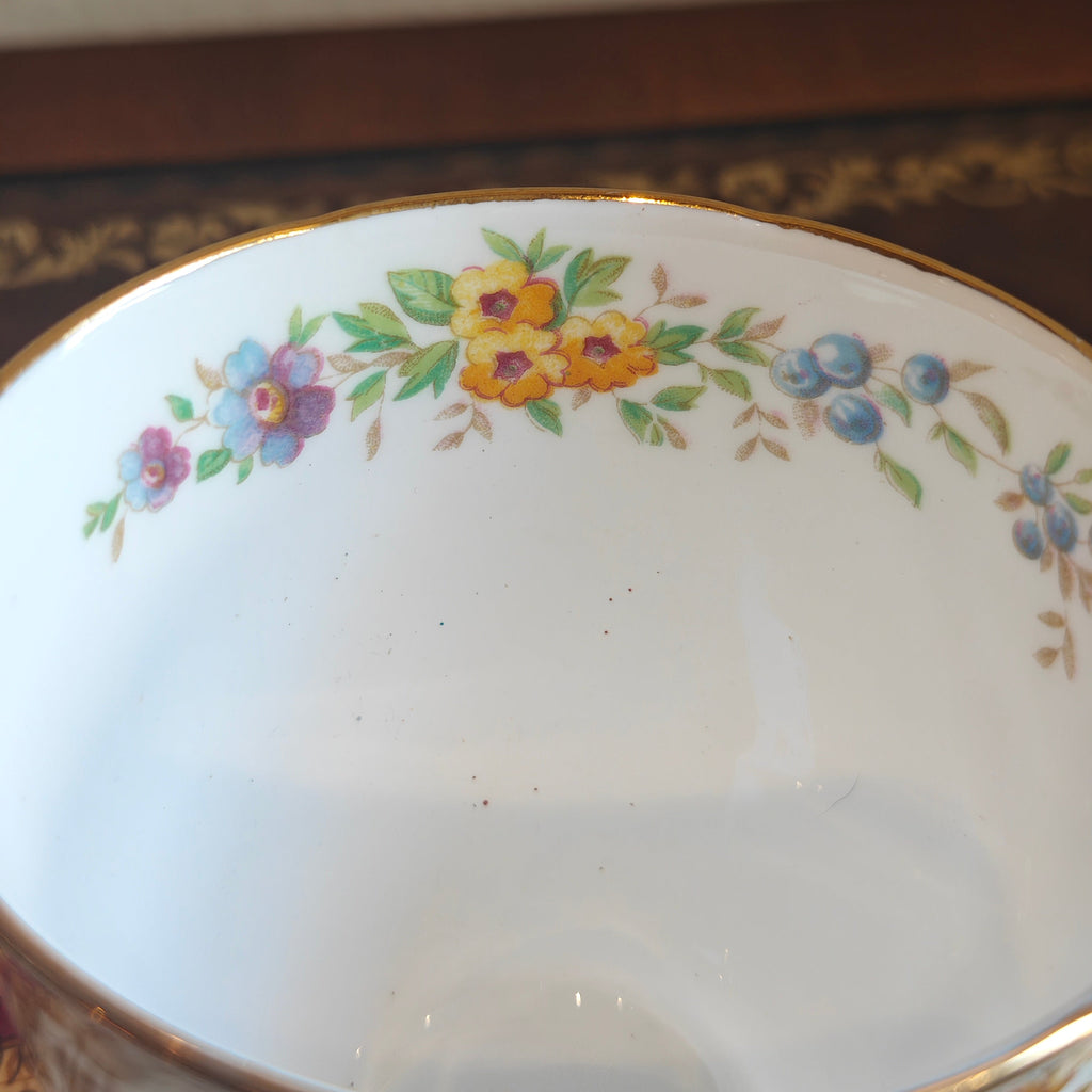 A close-up view of the inside of a white porcelain bowl or cup, decorated with a delicate floral border featuring yellow, blue, and purple flowers with green leaves and gold trim.