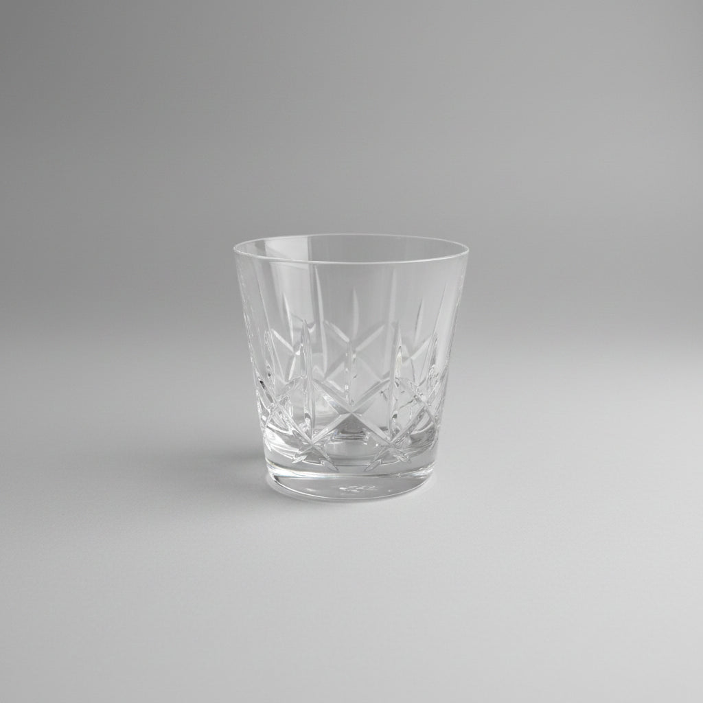 A clear cut-crystal tumbler glass with geometric facets, resting on a dark wooden tabletop.