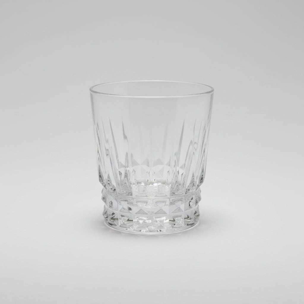 A clear cut-crystal tumbler with a faceted base, photographed on a dark wooden table.