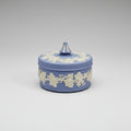 A heavy lidded Wedgwood jasperware jewellery box in blue and white colors, adorned with floral patterns, displayed on a lace-covered surface.