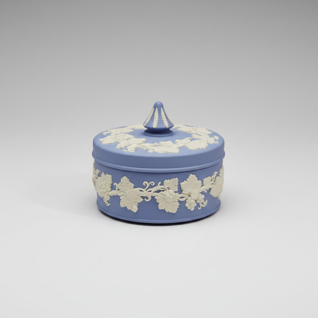 A heavy lidded Wedgwood jasperware jewellery box in blue and white colors, adorned with floral patterns, displayed on a lace-covered surface.